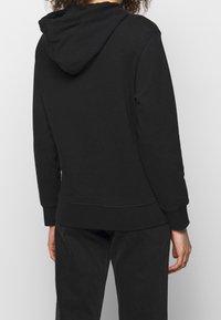 Svart hoodie med avslappnad passform, ribbade ärmslut och nederkant samt en mjuk textur. Har en minimalistisk design utan synliga logotyper.