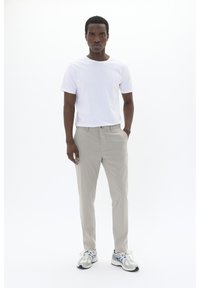 Pantalones gris claro con un patrón sutil, combinados con una camiseta blanca lisa. El modelo lleva zapatillas grises y azules.