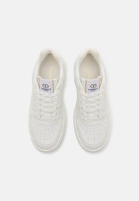 White leather sneakers with perforated details, flat laces, and a padded collar. Features gold accents and a logo on the tongue.