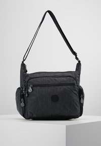 Borsa a tracolla nera con diversi scomparti con cerniera e tracolla regolabile, esposta su un piedistallo bianco.