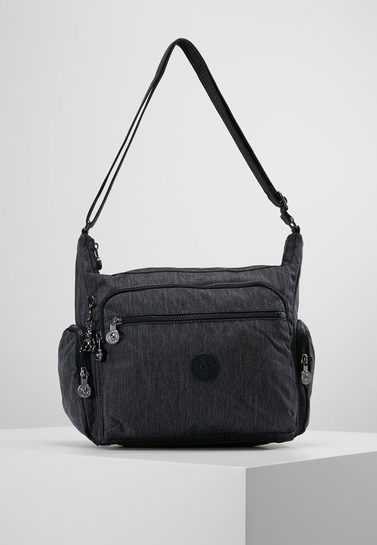 Borsa a tracolla nera con diversi scomparti con cerniera e tracolla regolabile, esposta su un piedistallo bianco.