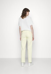 Calças amarelas claras com perna reta e dois bolsos traseiros, combinadas com uma camisa branca simples de mangas curtas. Ténis brancos completam o visual.