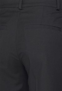 Black trousers with a textured fabric. Features two back pockets sewn with clean lines. Stitched waistband and straight cut design.