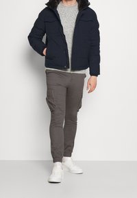 Granatowa pikowana kurtka z futrzanym kołnierzem, szary sweter oraz zwężane spodnie cargo. Białe trampki dopełniają stylizację, podkreślając casualowy charakter.