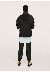 Sudadera negra con un corte oversize, con un bolsillo canguro. Capa sobre una camisa de color azul claro. Joggers negros de imitación cuero con puños elásticos. Zapatos negros.