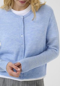 Cardigan bleu clair en tissu doux et texturé, avec un col rond, fermeture à cinq boutons et poignets à côtes.