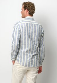 Camicia a righe in cotone blu chiaro e bianco con maniche lunghe, polsini con bottoni e colletto a punta. La vista dal retro mostra l'orlo arrotondato e una vestibilità morbida.