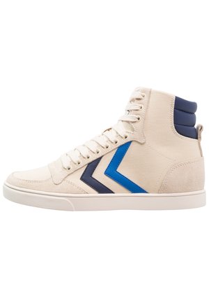 Baskets montantes beige avec lacets blancs, bandes chevron bleu marine et bleu sur le côté, et col de cheville rembourré bleu marine.