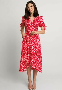 Czerwona sukienka w kwiaty, z krótkimi bufkowymi rękawami, wiązaniem w talii i zwiewnym dołem. Wykonana z lekkiego materiału z delikatnym połyskiem.
