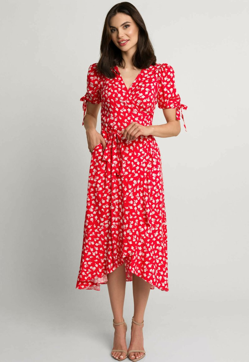 Czerwona sukienka w kwiaty, z krótkimi bufkowymi rękawami, wiązaniem w talii i zwiewnym dołem. Wykonana z lekkiego materiału z delikatnym połyskiem.