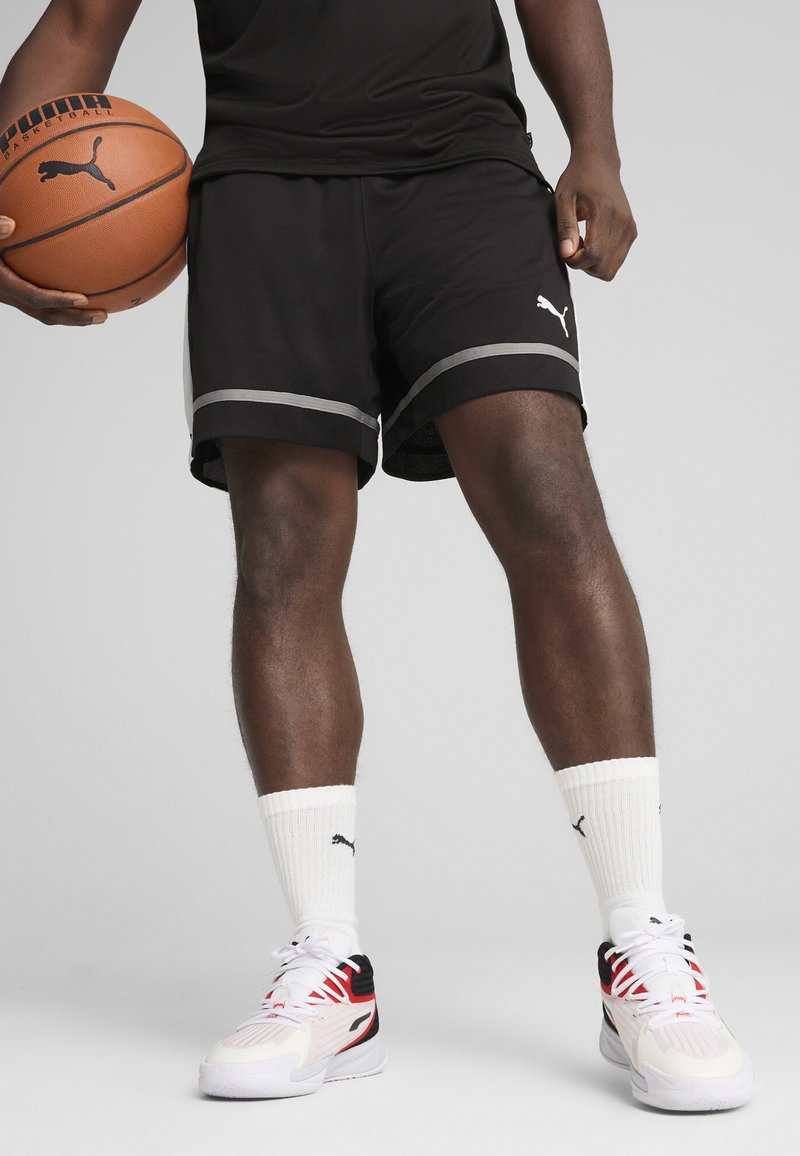 Shorts de basket noirs avec des accents gris, portés avec des chaussettes blanches et des baskets multicolores. Caractéristiques d'un tissu texturé et de détails de logo.