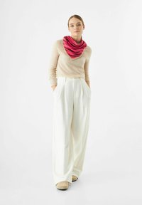 Lichtbeige gebreide trui gecombineerd met wijde witte broeken. Een roze en rode gegolfde driehoekige sjaal voegt kleur toe. Suède schoenen maken de look compleet.