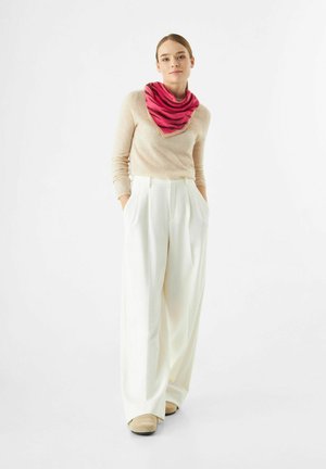 Hellbeige gestrickter Pullover kombiniert mit weiten weißen Hosen. Ein pink-rot gemusterter dreieckiger Schal bringt Farbe ins Outfit. Wildlederschuhe runden den Look ab.