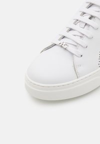 Baskets en cuir blanc avec un bout arrondi, des lacets plats, une semelle en caoutchouc texturée et un accent de logo en argent sur la languette.