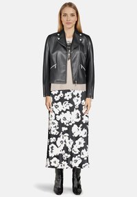 Veste de biker en cuir noir avec quincaillerie argentée, superposée à un haut beige et une jupe midi à imprimé floral noir, associée à des bottes hautes noires.