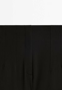 Pantalon noir taille haute avec des détails de coutures verticales et une fermeture éclair avant dissimulée.