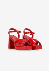 Sandalias de plataforma de charol rojo con tacones en bloque gruesos, múltiples tiras superpuestas y una correa para el tobillo con una hebilla circular.