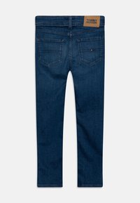 Vaqueros de mezclilla en azul oscuro. Con dos bolsillos traseros y una etiqueta de cuero marrón en la cinturilla con el nombre de la marca. Diseño de pierna recta, textura suave.