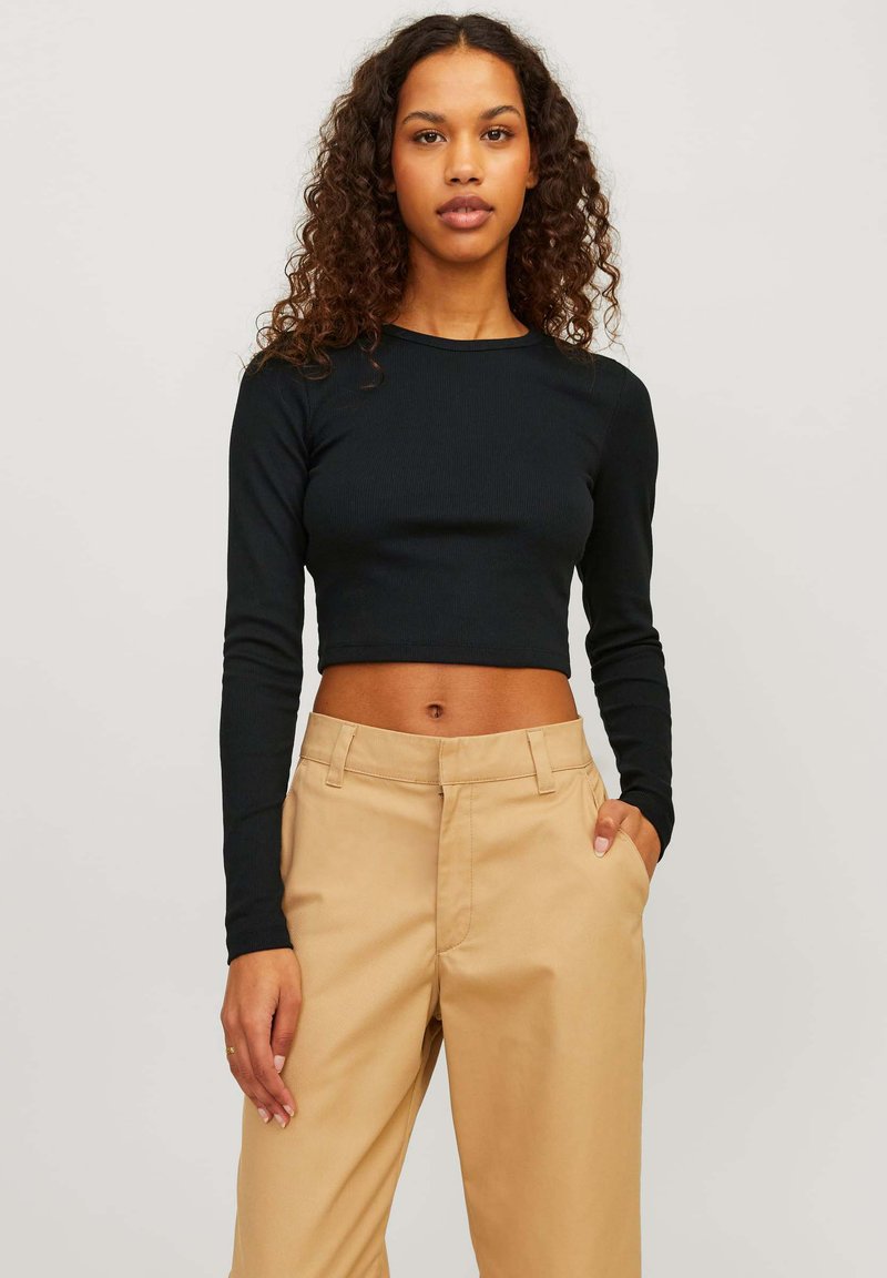 Zwart geribbelde langwerpige crop-top in combinatie met beige hoge taillebroek, voorzien van zijzakken en een gladde textuur.