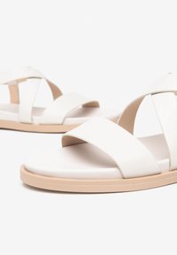 Sandali bianchi con ampie cinghie incrociate e suola piatta beige. Caratterizzati da una texture liscia e un design minimalista.