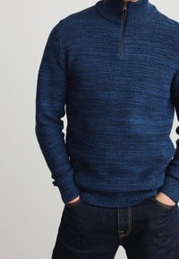 Marineblauer Strickpullover mit hohem Kragen und Viertel-Reißverschluss-Design. Mit strukturiertem Stoff sowie gerippten Bündchen und Saum. Trägt man mit dunklen Jeans.