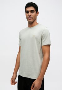 Ανοιχτό γκρι μπλουζάκι σε ελεύθερη εφαρμογή, κατασκευασμένο από απαλό βαμβάκι, με μικρό λογότυπο στη μπροστινή πλευρά και κλασικό λαιμόκοψη τύπου crew.