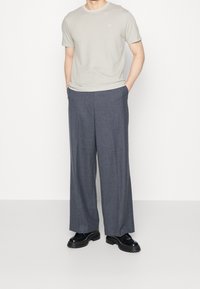 Jasnoszara koszulka z krótkim rękawem i okrągłym dekoltem, zestawiona z ciemnoszarymi spodniami typu wide-leg oraz czarnymi sznurowanymi butami. Styl minimalistyczny.