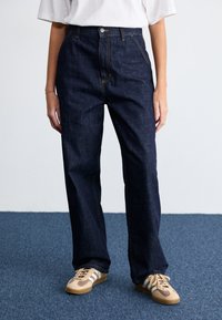 Dark blue, high-waisted denim jeans with a straight leg design. Detailed with yellow stitching and a front button closure.