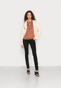 Jaqueta de motoqueiro de couro bege claro por cima de uma blusa de cor ferrugem com padrão floral. Jeans skinny pretos e mules pretos de salto completam o visual.