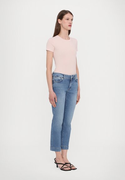 Top rosa claro de malha com mangas curtas combinado com jeans azul de cintura média, com pernas retas e um leve desbotado, complementado por sandálias pretas com tiras.