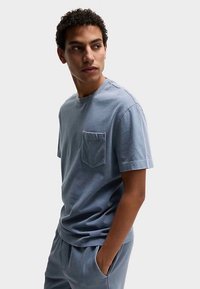 Lyseblå bomuld T-shirt med rund hals, korte ærmer og en venstre brystlomme. Blød tekstur, afslappet pasform, minimalistisk design.