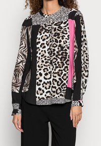 Blus med långa ärmar som har blandade djurmönster i svart, vitt och rosa, med en texturerad krage och knäppning fram.