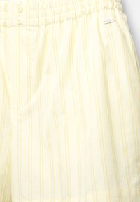 Gelb gestreifte Shorts aus einem weichen Stoff, mit einem elastischen Bund und zwei Knöpfen. Kleine Etikett-Details am Bund.