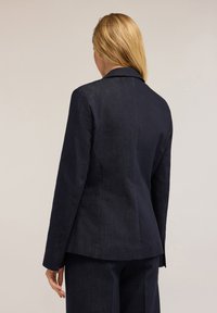 Sacou din denim bleumarin cu o croială ajustată, rever tăiat și textură subtilă. Include un spate cu ventilație și mâneci lungi.