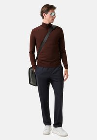 Brauner Zip-Kragen-Pullover, marineblaue Hose, weiße Sneaker und eine schwarze Umhängetasche. Reflexion-Sonnenbrille verleiht einen modernen Akzent.