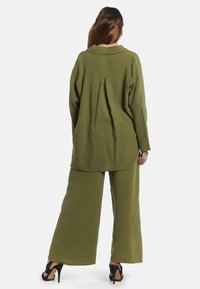 Olivgrön, texturerad, löst sittande blus och byxor med vida ben i ett krinklat tyg. Styld med svarta högklackade sandaler.
