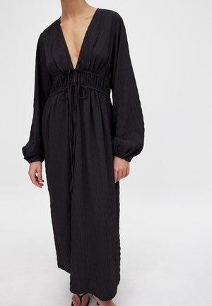 Schwarzes Kleid mit langen Ärmeln, tiefem V-Ausschnitt und taillierter Taille. Hergestellt aus strukturiertem Stoff, mit Kordelzug und fließender Silhouette.