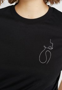 Černé bavlněné tričko s kulatým výstřihem. Obsahuje bílé, minimalistické liniové kreslení na levé straně hrudi. Měkká textura.
