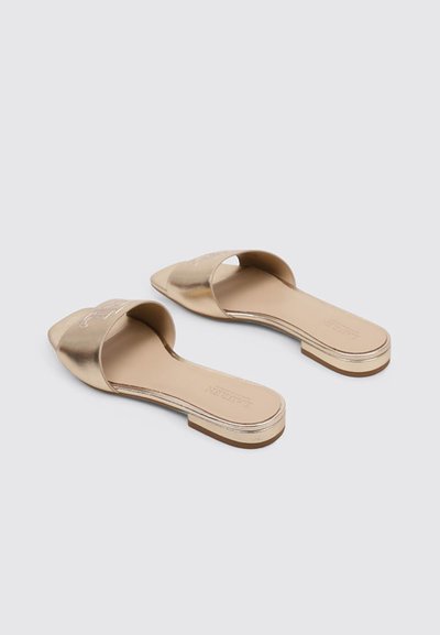 Sandalias planas metálicas doradas con una amplia tira superior, textura suave, suela plana y un diseño minimalista.