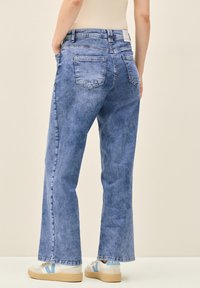 Ljusblå, vida jeans med en urtvättad textur. Har två bakfickor och hög midja, tillsammans med vita och blå sneakers.