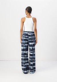 Wijde broek in blauwe tie-dye patronen, lichtgewicht stof, hoge taille, rechte snit, met zakken aan de achterkant, gecombineerd met een witte tanktop.