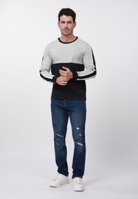 Dugačko majica s blok bojama u sivoj i crnoj, s mekanim tkaninom, rebrastim manšetama i malim logotipom. Upareno s trapericama s poderotinama.