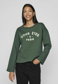 Sudadera verde con escote redondo y mangas largas. Presenta el texto "VOUS ÊTES À PARIS" en letras de color crema en la parte frontal.