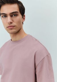 Svetle růžové tričko z bavlny s kulatým výstřihem a krátkými rukávy. Měkká, hladká textura s volnějším střihem. Minimalistický design.