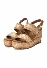 Sandali con zeppa realizzati in materiale di paglia intrecciata in beige chiaro, con due ampie cinghie, un accento metallico sottile e una suola platform testurizzata.