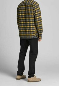 Jeans neri abbinati a una camicia di flanella a quadri gialli e grigi, con maniche lunghe, colletto a bottoni e un taglio rilassato. Scarpe beige chiaro.