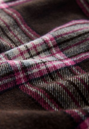 Volnena tkanina s temno rjavo podlago, okrašena z rožnato, sivo in črno karo vzorcem. Mehka tekstura z vidnimi vlakni in podrobnostmi tkanine.