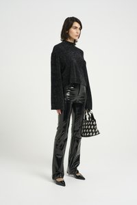 Črn, bleščeč oversized pulover z dolgimi rokavi, v kombinaciji z bleščečimi črnimi hlačami iz umetnega usnja, ki se širijo navzdol, in majhno torbico v houndstooth vzorcu.