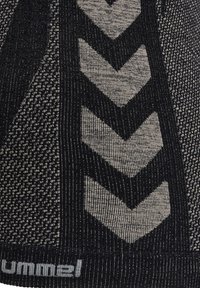 Strukturiertes schwarzes Stoffmaterial mit Chevron-Mustern in Hellgrau. Verfügt über ein geripptes Design und ein auffälliges Logo am unteren Rand.