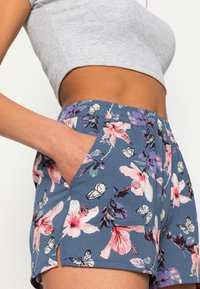 Blommiga shorts i ett blått tyg, med en blandning av rosa och vita blommor samt fjärilar. Inkluderar sidofickor och en avslappnad passform.